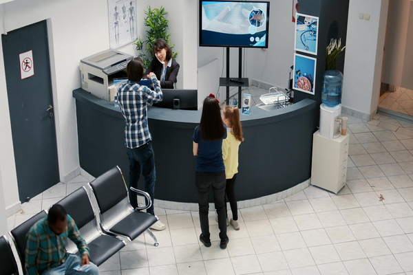 Patients checking in at modern medical clinic reception desk.