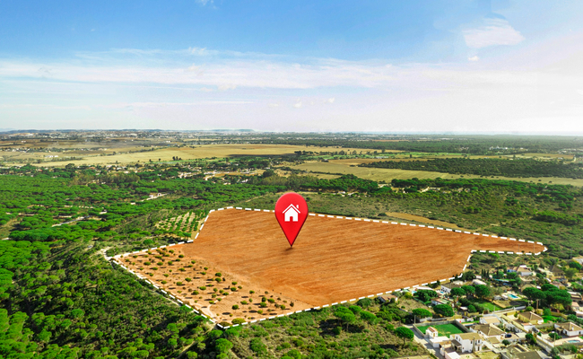 Aerial view of a large undeveloped plot of land outlined in white, marked with a red location pin icon, symbolizing the early stage of the land entitlement process.